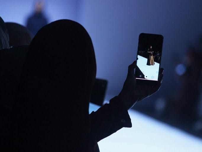 Person filmt einen Laufsteg mit dem Smartphone bei einer Modenschau